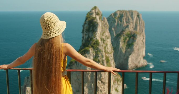 Woman with straw hat enjoying view of Faraglioni rock formations in Capri