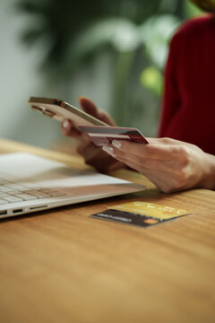 Woman holding a credit card and smartphone while shopping online with a laptop, representing secure digital payment and e-commerce.