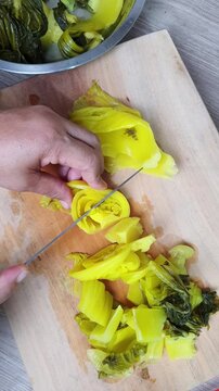 Slicing pickled mustard greens on a wooden cutting board with a knife. Prepping traditional Asian ingredients for cooking a savory homemade recipe