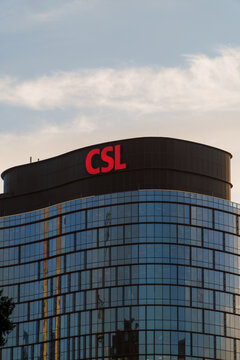 The prominent red CSL logo illuminates the curved top of a modern glass office building under a bright, cloudy sky.