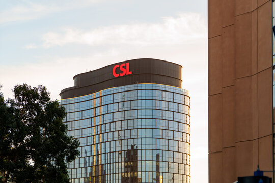 Modern CSL Pharmaceutical Company Building Features a Striking Curved Glass Facade and Prominent Red Logo Under a Bright Sky.