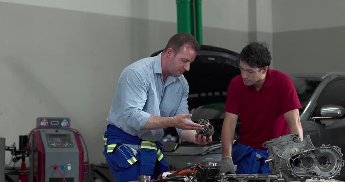 Senior engineer and technician inspecting electric vehicle motor component with high voltage cable