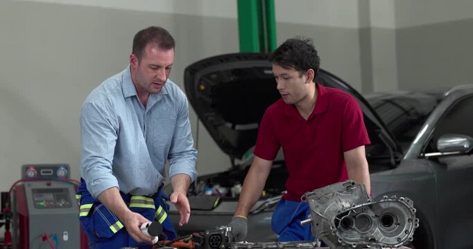Senior engineer and technician inspecting electric vehicle motor component with high voltage cable