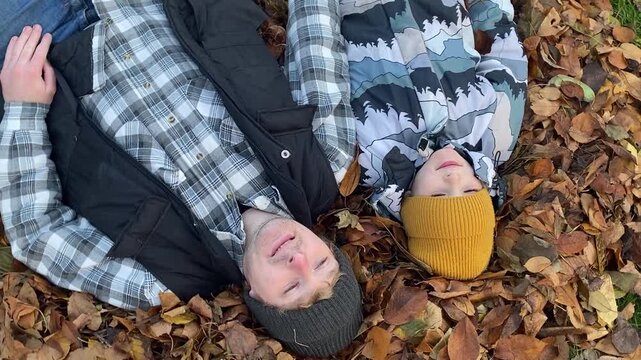 Young dad with daughter and son of primary school age in warm autumn clothes enjoying quality time together in the yard among fallen golden leaves. Cozy family autumn concept. The beauty of fall .