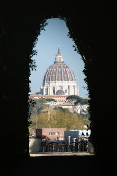 The dome of St. Peter's Basilica framed by a garden hedge tunnel through the Aventine Keyhole in Rome, Italy