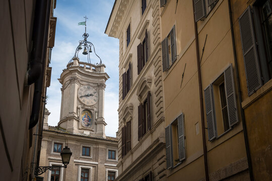 The historic Borromini clock tower framed by traditional Roman facades with wooden window shutters in Rome, Italy