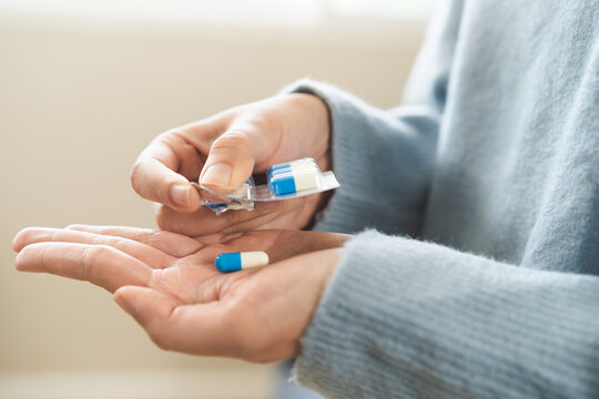 Sick asian young woman, girl taking tablet pill capsule out from blister pack, painkiller medicine for stomach pain, head ache, pain for treatment, take drug or vitamin at home, health care concept.