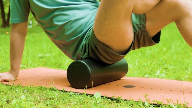 man performs myofascial release using a foam roller on a mat in a green park. This self-massage helps relieve muscle tension for post-workout recovery and rehabilitation. High quality 4k footage
