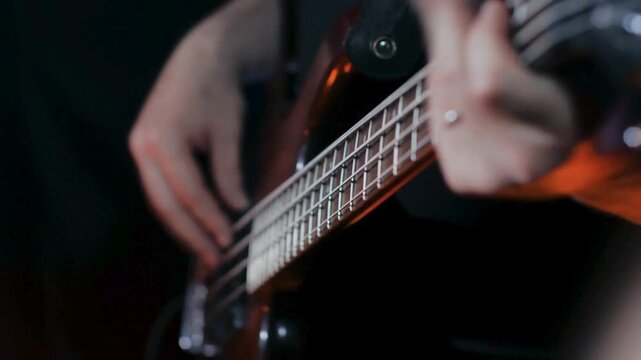 Close up bassist plucking electric bass strings during moody concert performance