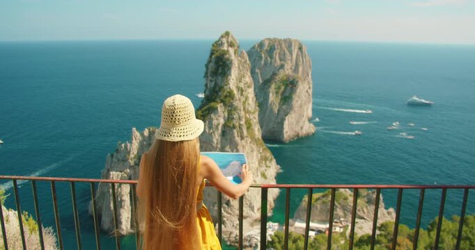 Woman holding map above dramatic Faraglioni sea cliffs at coastal viewpoint in Capri