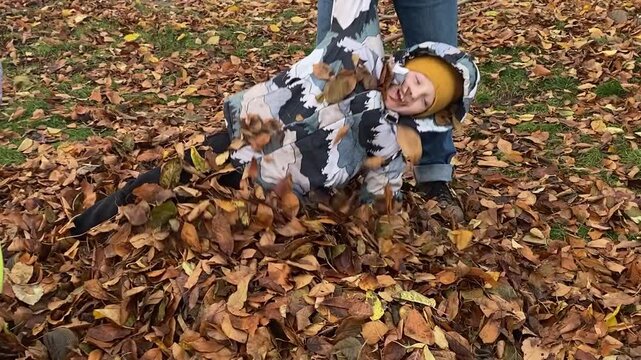 Young dad with daughter and son of primary school age in warm autumn clothes enjoying quality time together in the yard among fallen golden leaves. Cozy family autumn concept. The beauty of fall .
