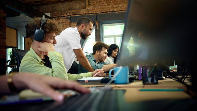 Employees working together at computer screens in modern open plan office. Concept of digital teamwork, software collaboration and coordinated office productivity.