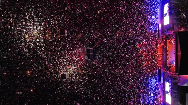 Aerial top view of crowd at night music concert. People gathered at festival outdoor stage with lights and screens, 4k
