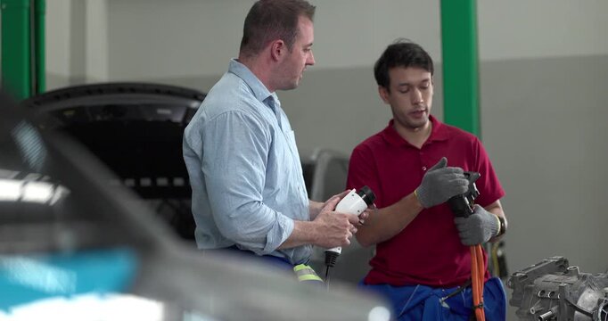 Senior engineer and technician inspecting electric vehicle motor component with high voltage cable
