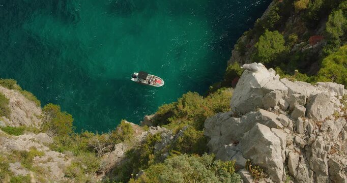 Tour boat gliding below rocky seaside cliff with seagull over clear turquoise water