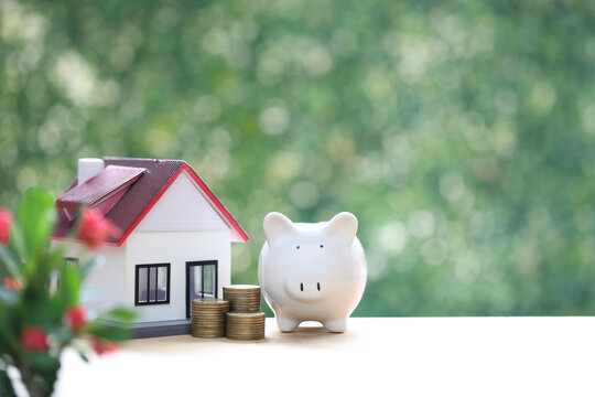 House model with piggy bank and stacked coins, concept of saving money for real estate, property investment, mortgage and future financial planning.
