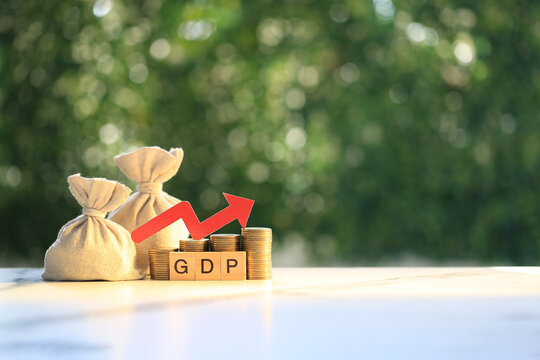 GDP (Gross Domestic Product) text on wooden blocks with stacked coins, money bags and a red upward arrow, concept of economic growth, financial development and investment success.