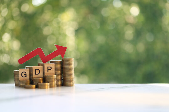 GDP (Gross Domestic Product) text on wooden blocks with stacked coins and a red upward arrow, concept of economic growth, financial development and investment success.