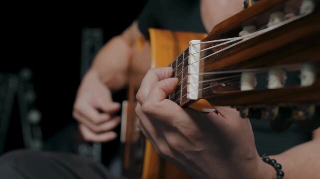 Skilled guitarist plays classical acoustic guitar with expressive hands in dark studio