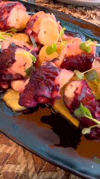 Appetizing gourmet dish featuring grilled octopus tentacles with fried potatoes and fresh microgreens, elegantly served on a dark plate in a restaurant for a fine dining experience