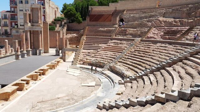Panoramic view of the ancient roman theatre in cartagena, murcia, spain, revealing the archaeological ruins of the cavea, orchestra, and scaenae frons on a sunny day with tourists visiting