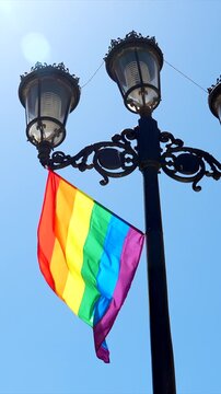 Colorful rainbow lgbt flag hanging on a classic black lamppost, gently waving in the wind against a clear blue sky during a sunny day in the city of cartagena in murcia, spain