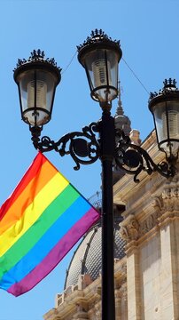 Colorful lgbtq plus pride flag fluttering in the wind on a vintage lamppost in a historic european city square, celebrating diversity, equality, and human rights on a sunny day in cartagena, spain
