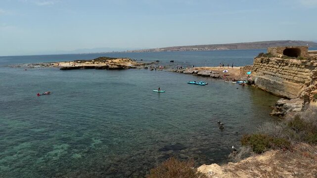 Beautiful coastal landscape of tabarca island in spain with tourists swimming and kayaking in the clear turquoise water of the mediterranean sea during a sunny summer day