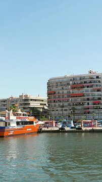Tourist ferry departing from the bustling port of santa pola, alicante, with city buildings and palm trees lining the sunlit waterfront during a perfect summer day for a trip to tabarca island