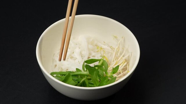 Using chopsticks to put fresh herbs and bean sprouts in a bowl of Vietnamese Pho.