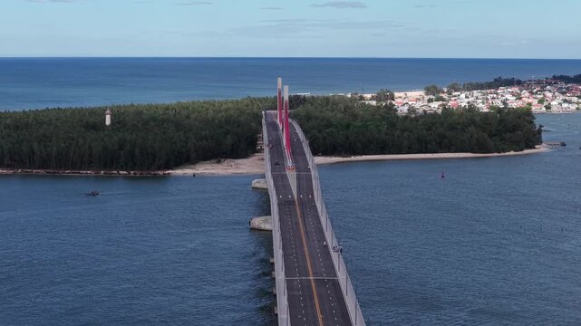 Drone orbits around the main tower of the Thuan An Bridge, revealing the red cable stays fanning out against blue sky and turquoise waters below.