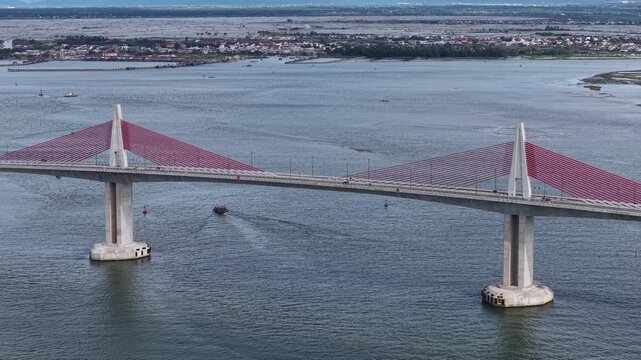 Low aerial perspective over the lagoon water surface captures the Thuan An Bridge spanning overhead, its towers and cables creating a dramatic silhouette.