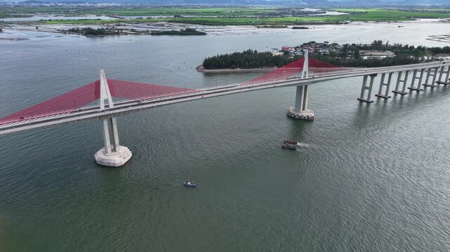 Top-down drone perspective shows the red line of the Thuan An Bridge cutting across the vast lagoon, with green islands and blue water creating a vivid pattern.