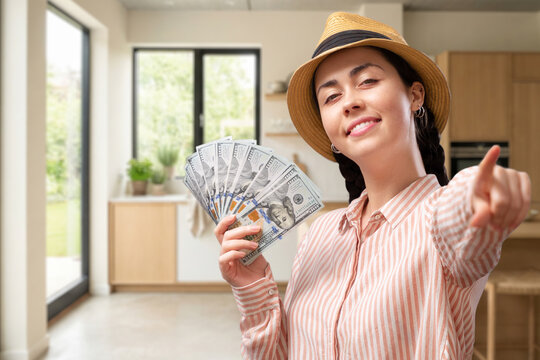 Smiling young Caucasian woman showing dollar bills while standing in a modern new kitchen and looking at the camera. Home financing, mortgage approval, renovation loan, real estate investment