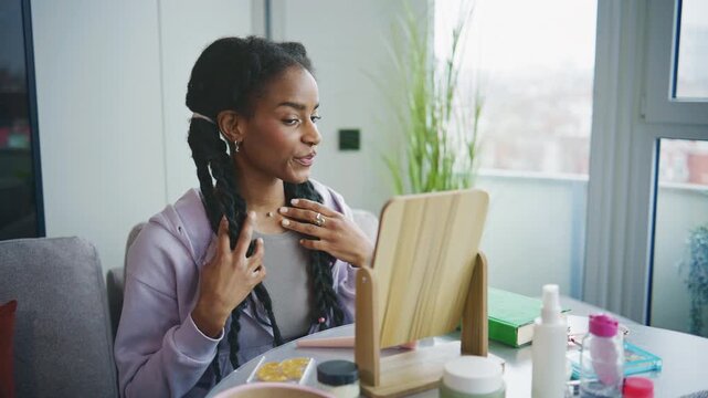 Young woman applies skincare products in front of a mirror during the day at home while sitting at a table