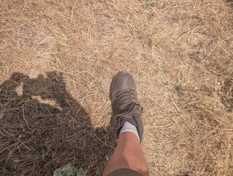 Scarpa da trekking su terreno secco e polveroso, con vegetazione rada e l&rsquo;ombra del fotografo proiettata sul suolo sotto luce intensa