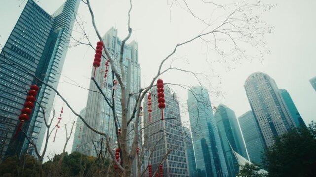 Upward shot of red Chinese New Year lanterns hanging from bare winter tree branches in Lujiazui Central Green, Shanghai, with the Lujiazui financial district skyscrapers rising through pale winter haz