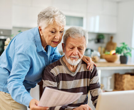 Senior couple checking bills and calculating expenses using a laptop at home, debt taxes concept, worried married elderly couple