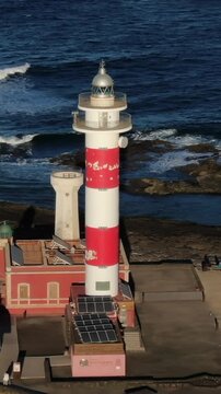 Dramatic aerial perspective of the iconic red and white Toston Lighthouse standing against the deep blue Atlantic Ocean in Fuerteventura