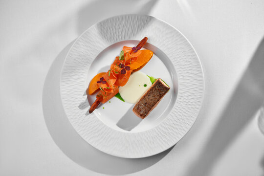 Seared salmon with carrot ribbons on white plate. Sunny minimalist fine dining table setting.