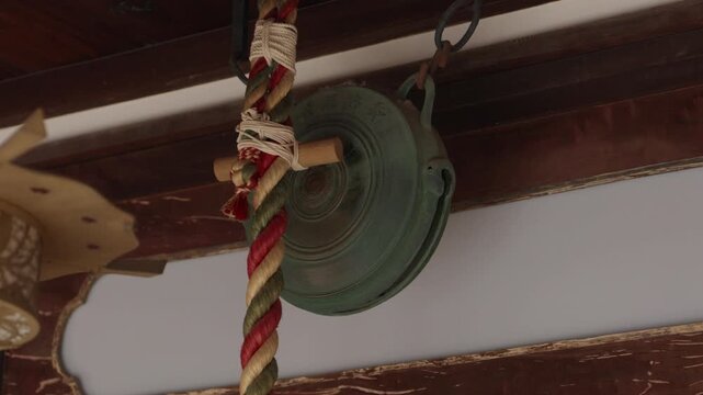 Weathered bronze prayer bell with a colorful braided rope hanging at a Japanese shrine offering hall