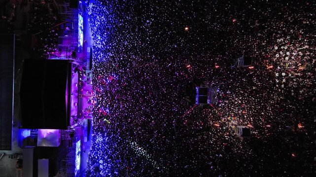 Aerial top view of crowd at night music concert. People gathered at festival outdoor stage with lights and screens, 4k