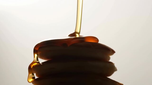 Amber syrup flowing over stacked pancakes with glossy pooling, rich texture, and warm backlit highlights creating appetizing breakfast dessert appeal, with syrup, pancake, stack, flowing detail