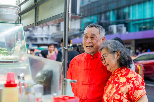 Elderly couple smiles while choosing food at street vendor in a busy city setting in the evening