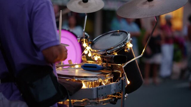 Street performer playing a drum set decorated with glowing lights during an outdoor concert, entertaining public