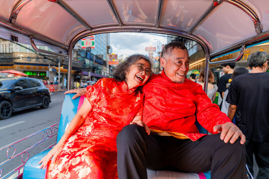 Elderly couple enjoys a ride in a tuk-tuk while wearing traditional clothing in a busy city street