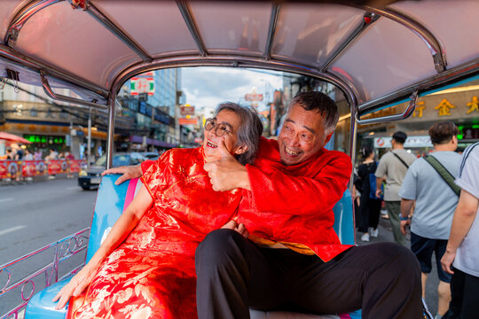 Elderly couple enjoying a ride in a tuk-tuk on a busy street in Bangkok during daytime