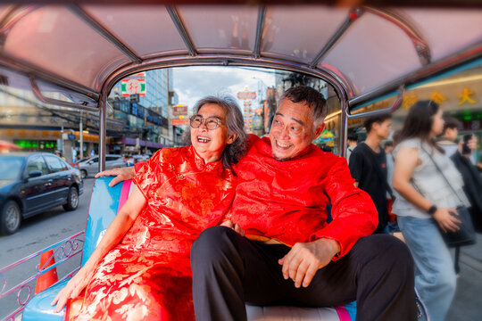 Older couple enjoys a ride in a transportation vehicle while wearing traditional clothing during a busy street scene