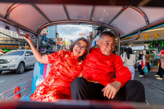 Elderly couple enjoys a ride in a tuk-tuk on a busy street in Bangkok during the day