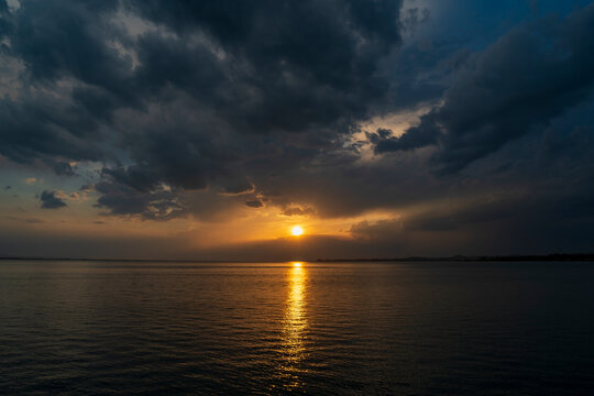 Dramatic sunset over Lake Constance seen from the Austrian shore in Bregenz, Vorarlberg, with the golden sun breaking through dark storm clouds and reflecting on the calm water surface